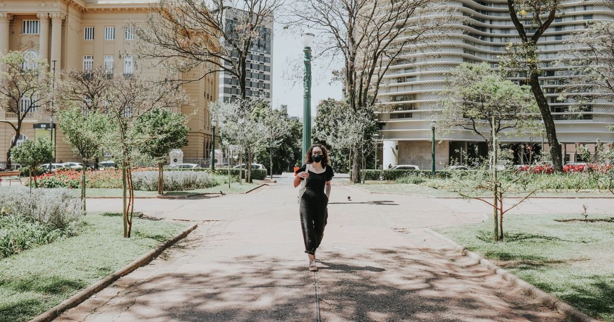 Mulher caminhando por uma alameda arborizada no parque